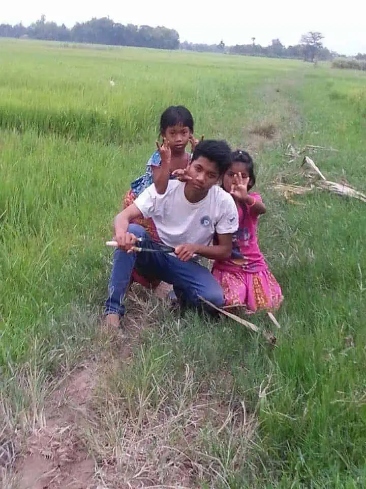 Phare Circus staff Kimhak Hun poses with sisters next to rice field - Puok District, Siem Reap
