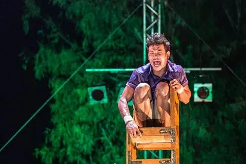 Frightened Phare Circus performer on a chair tower on the outdoor stage in the show "Chills"
