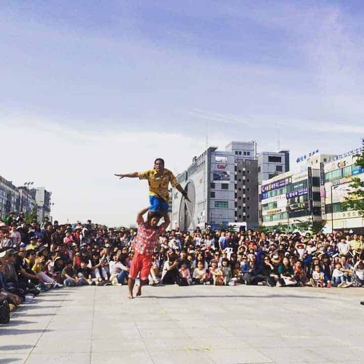 Phare Circus perform live outdoors, performer standing on the sholder of another who is running, audience surrounds