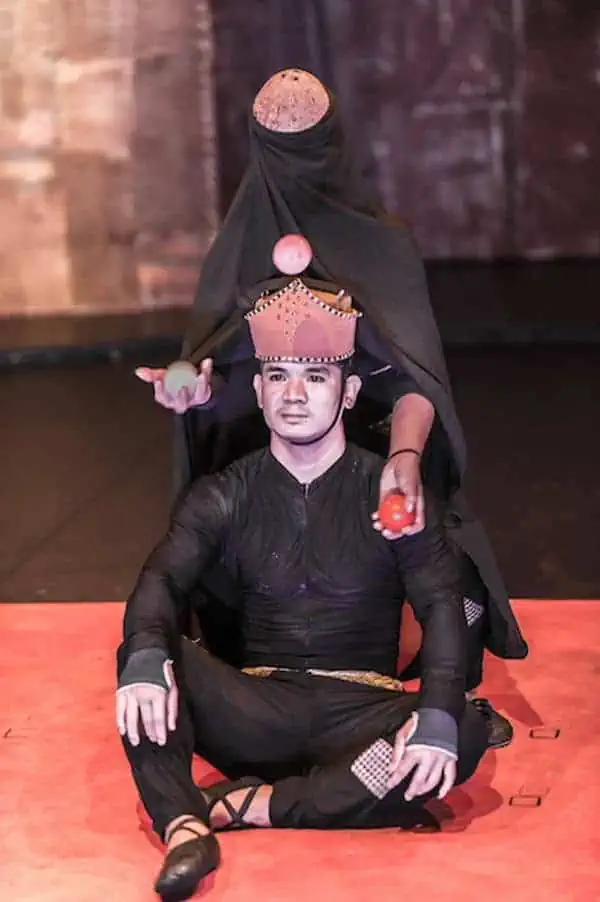 Phare Circus live show "Influence" - juggler with black robe and coconut mask with seated king