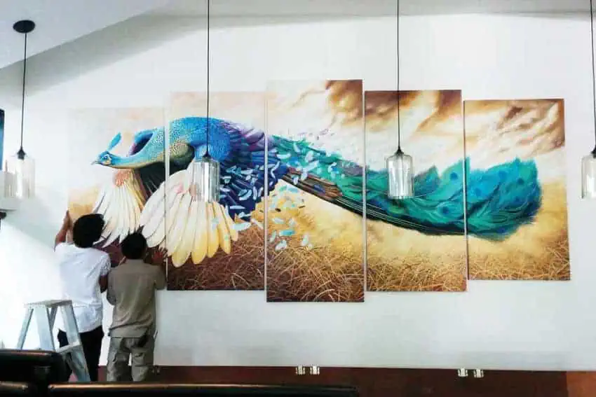 Artist Channy Chhoeun hangs peacock painting at Aviary Hotel Siem Reap for solo exhibit