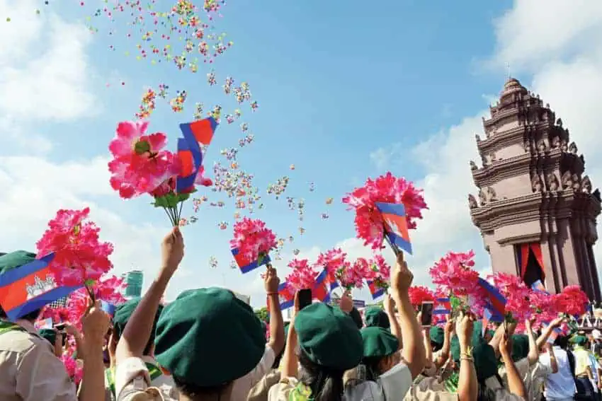 Cambodian Independence celebration in Phnom Penh - residents hold up flowers and flags at Independence Monument