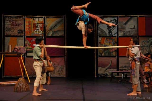 Phare circus performance, female performer does handstand on bamboo poles held by 2 men on their shoulders
