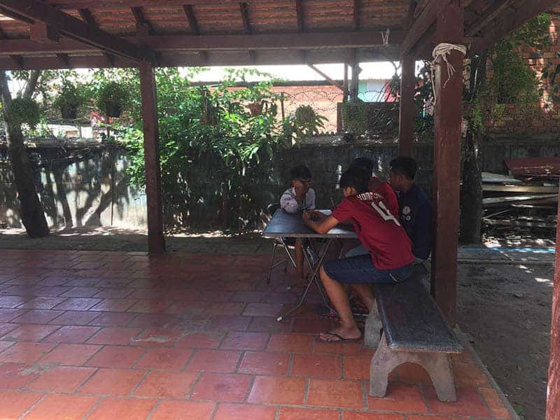5 male Students chatting on the patio, seated at a metal table