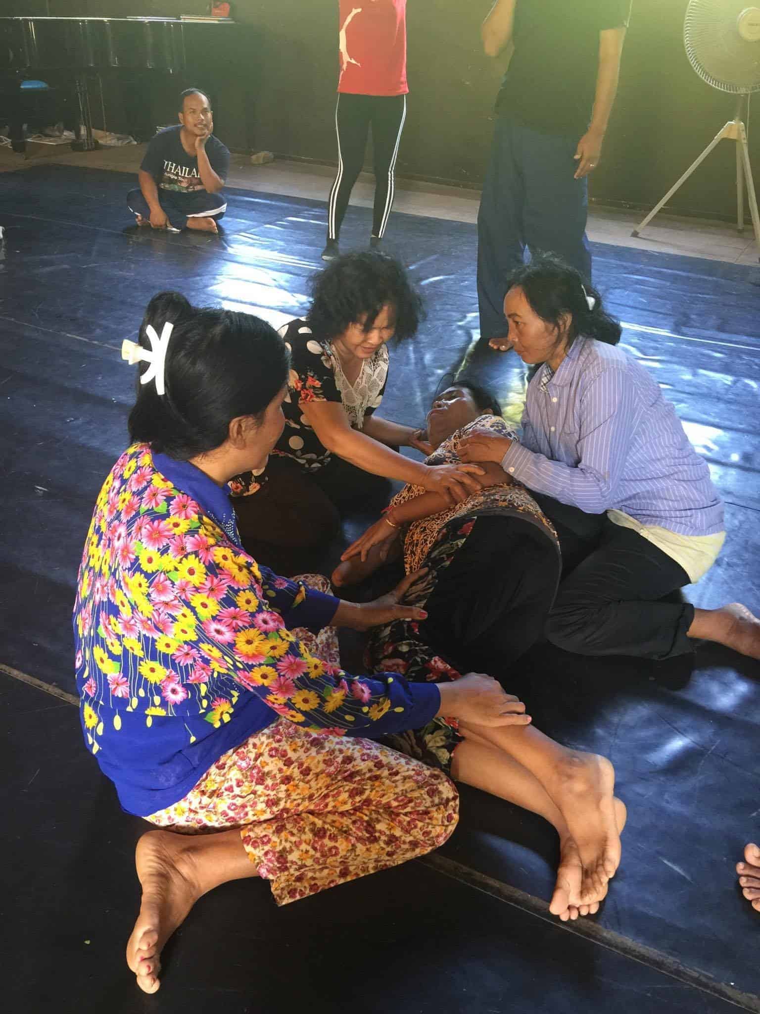 Theater in Cambodia - 3 women seated around another laying on the floor in theater performance