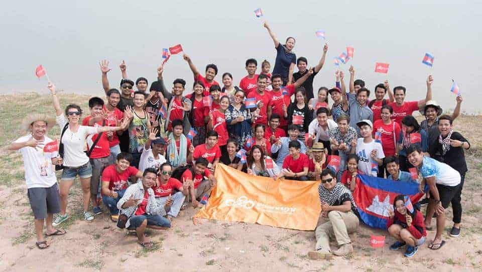 Phare Circus artists and staff take group photo at water's edge of West Baray with flags of Cambodia and Phare