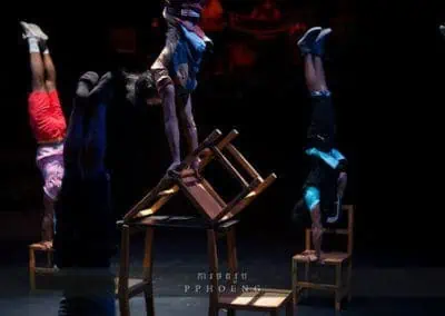 Phare Circus performance "Chills": performers in student costume do handstands on wooden chairs