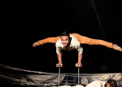 Phare Circus show "Same Same But Different" - cultural differences: smiling male performer suspended horizontal on balancing sticks