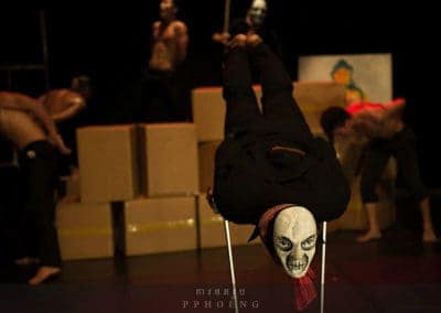 Phare Circus show "Sokha": performing artist in black and skull mask on balancing sticks with blurred background