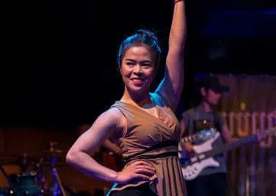 Phare Circus show "Khmer Metal": smiling female dancer with one hand held up. musicians in the background